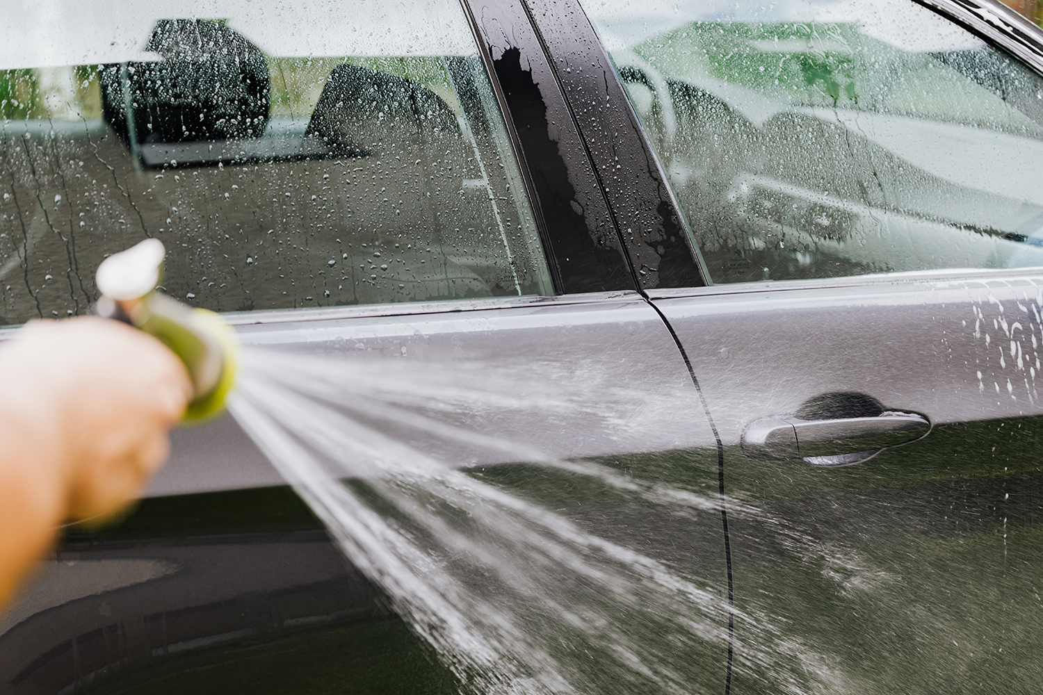 Bielym octom je možné umývať okná na aute a odstrániť staré nálepky a lepidlo. Muž na obrázku umýva pomocou hadice zvyšný ocot z boku auta.